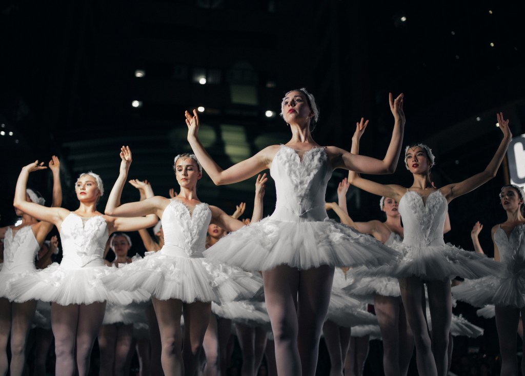 Image of a group of ballet dancers in white tutus, taken in motion.
