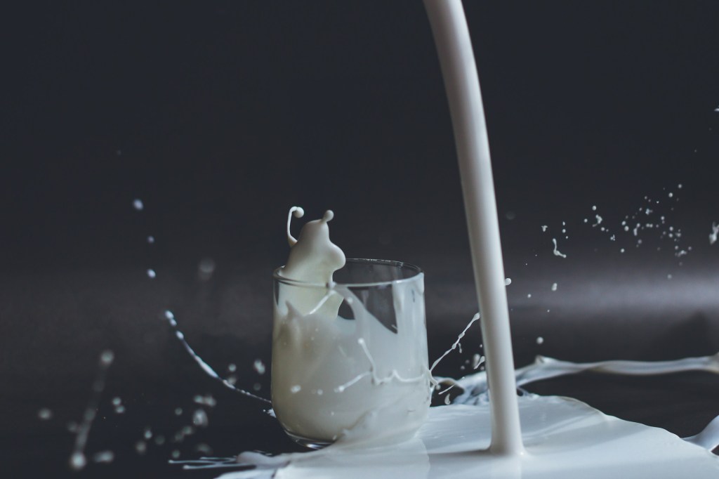 Milk being poured onto a table next to a glass.